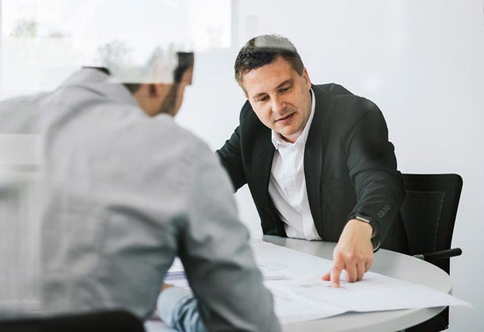 Ingenieur bespricht mit einem Kunden die nächsten Projektschritte und zeigt dabei auf den Projektplan.